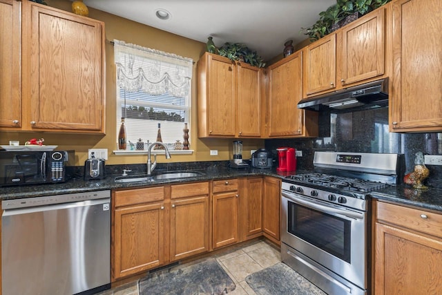 kitchen featuring dark stone countertops, a sink, stainless steel appliances, under cabinet range hood, and backsplash