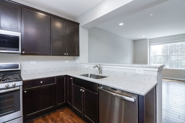 kitchen with light stone counters, a peninsula, dark wood-style floors, stainless steel appliances, and a sink