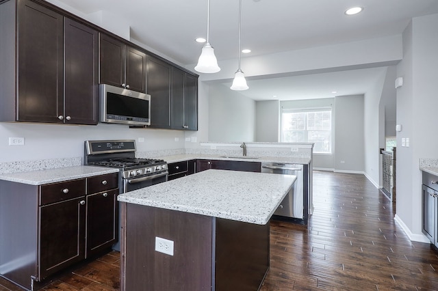 kitchen featuring a sink, dark brown cabinetry, appliances with stainless steel finishes, a peninsula, and dark wood-style flooring