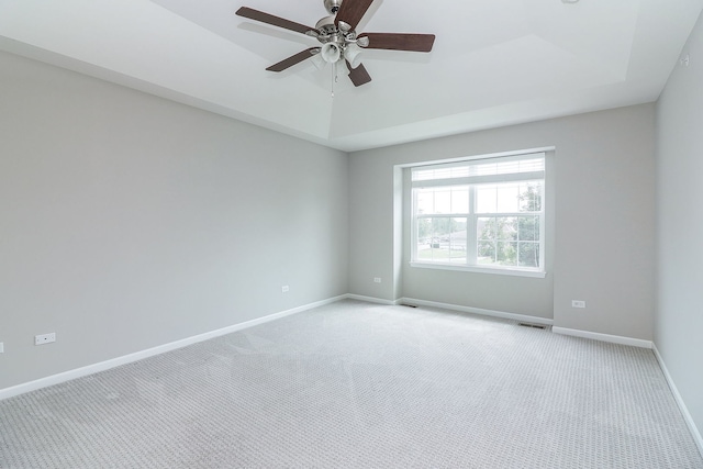 empty room featuring a tray ceiling, visible vents, baseboards, and light carpet