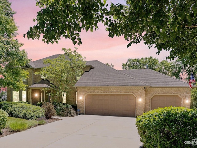 view of front facade featuring brick siding, an attached garage, concrete driveway, and roof with shingles