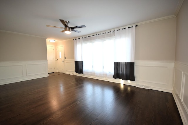 empty room featuring a wainscoted wall, visible vents, ceiling fan, dark wood-type flooring, and crown molding