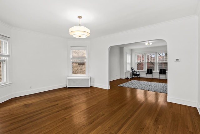 unfurnished room featuring arched walkways, ornamental molding, radiator heating unit, and wood finished floors