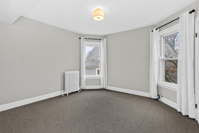 spare room featuring baseboards, radiator, and dark carpet