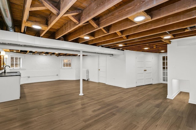 basement with a sink, plenty of natural light, dark wood-type flooring, and radiator heating unit