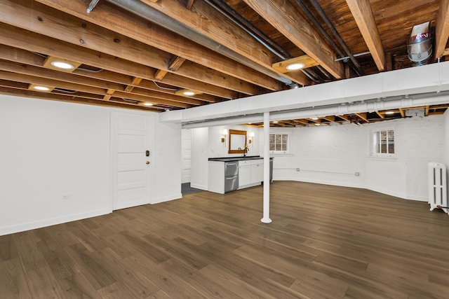 basement featuring radiator heating unit, dark wood-type flooring, and baseboards