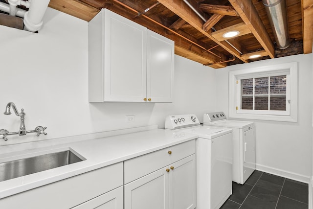 laundry room with baseboards, dark tile patterned flooring, separate washer and dryer, cabinet space, and a sink