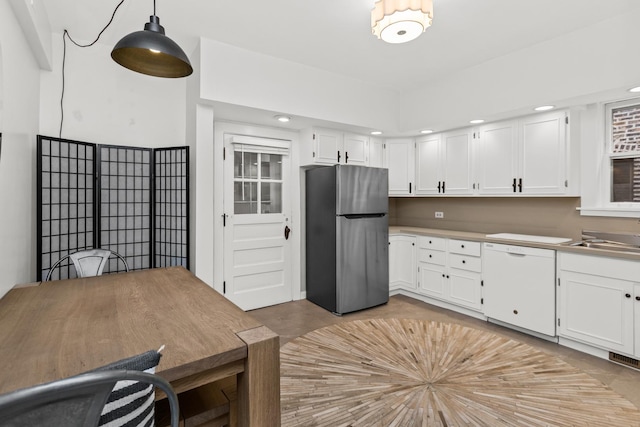 kitchen with white cabinets, white dishwasher, freestanding refrigerator, and a sink