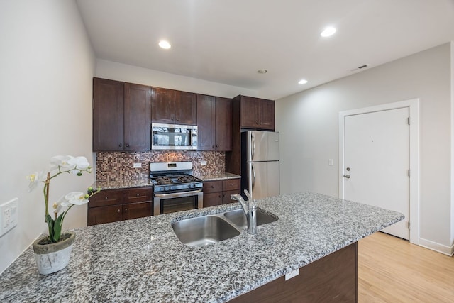 kitchen featuring a sink, decorative backsplash, stainless steel appliances, dark brown cabinets, and light wood-style floors