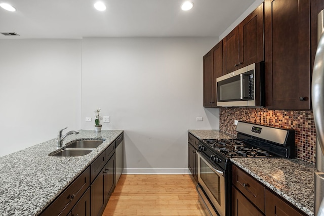 kitchen featuring tasteful backsplash, light wood-style flooring, appliances with stainless steel finishes, stone countertops, and a sink