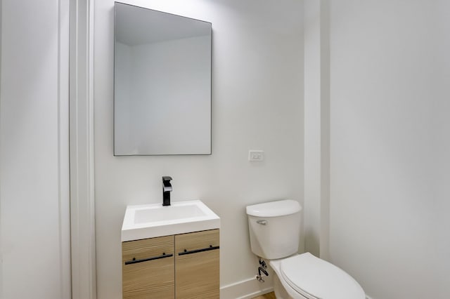 half bath featuring baseboards, toilet, and vanity