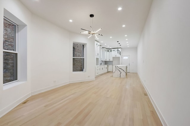 unfurnished living room with baseboards, recessed lighting, light wood-style flooring, a notable chandelier, and a sink