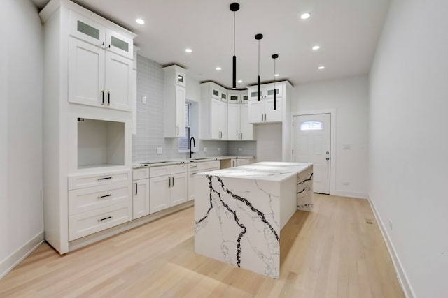 kitchen with backsplash, a kitchen island, light wood-style floors, and light stone countertops