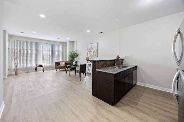 kitchen featuring light stone countertops, freestanding refrigerator, light wood-style floors, a sink, and baseboards