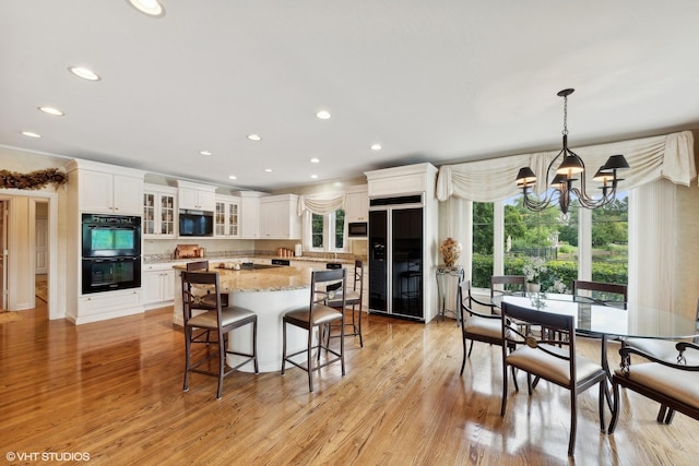 kitchen featuring light wood-style flooring, black appliances, white cabinets, and an inviting chandelier