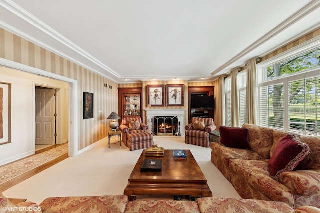 living room featuring wallpapered walls, crown molding, baseboards, a lit fireplace, and carpet flooring