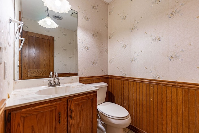 bathroom featuring a wainscoted wall, toilet, wallpapered walls, and vanity