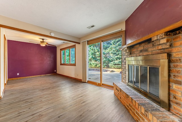 unfurnished living room with visible vents, a textured ceiling, wood finished floors, baseboards, and a brick fireplace