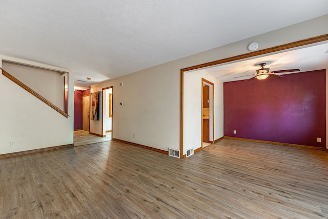 empty room featuring visible vents, a ceiling fan, wood finished floors, stairway, and baseboards