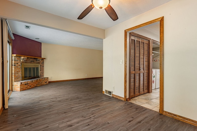 unfurnished living room with wood finished floors, a ceiling fan, visible vents, baseboards, and a brick fireplace