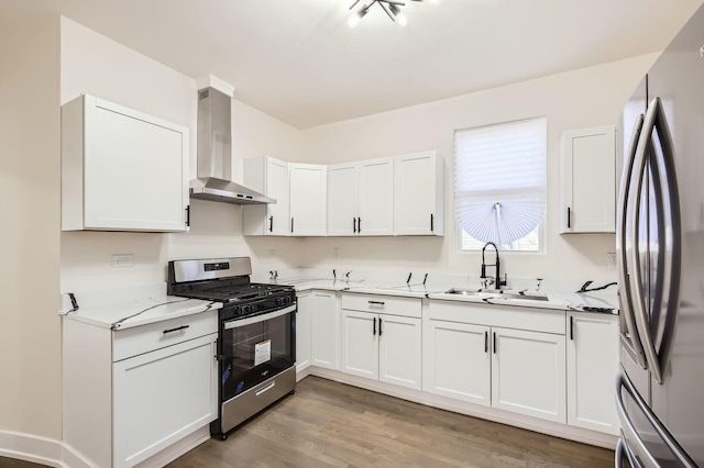 kitchen featuring light wood-type flooring, a sink, white cabinetry, stainless steel appliances, and wall chimney range hood