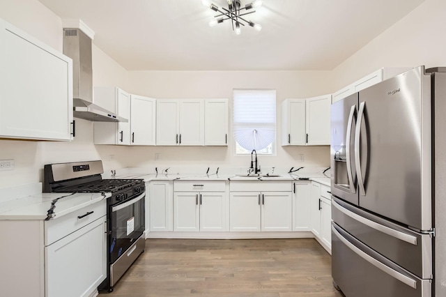 kitchen featuring light wood-style flooring, a sink, white cabinets, appliances with stainless steel finishes, and wall chimney exhaust hood