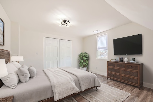 bedroom with wood finished floors, visible vents, baseboards, lofted ceiling, and a closet