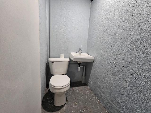 bathroom featuring toilet, a textured wall, and a sink