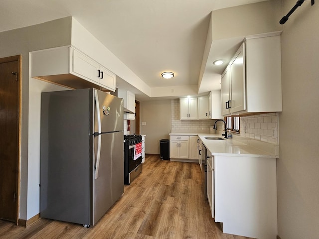 kitchen featuring a sink, range with gas stovetop, freestanding refrigerator, light wood-style floors, and decorative backsplash