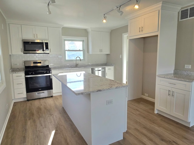 kitchen featuring a sink, stainless steel appliances, white cabinetry, light wood-type flooring, and backsplash