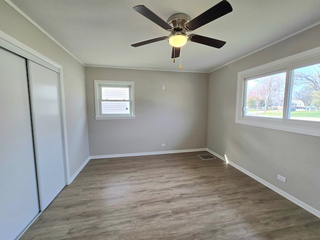 unfurnished bedroom featuring visible vents, a closet, wood finished floors, and crown molding