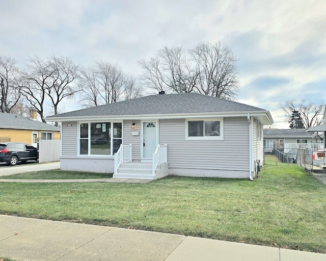 view of front facade with a shingled roof, a front yard, and fence