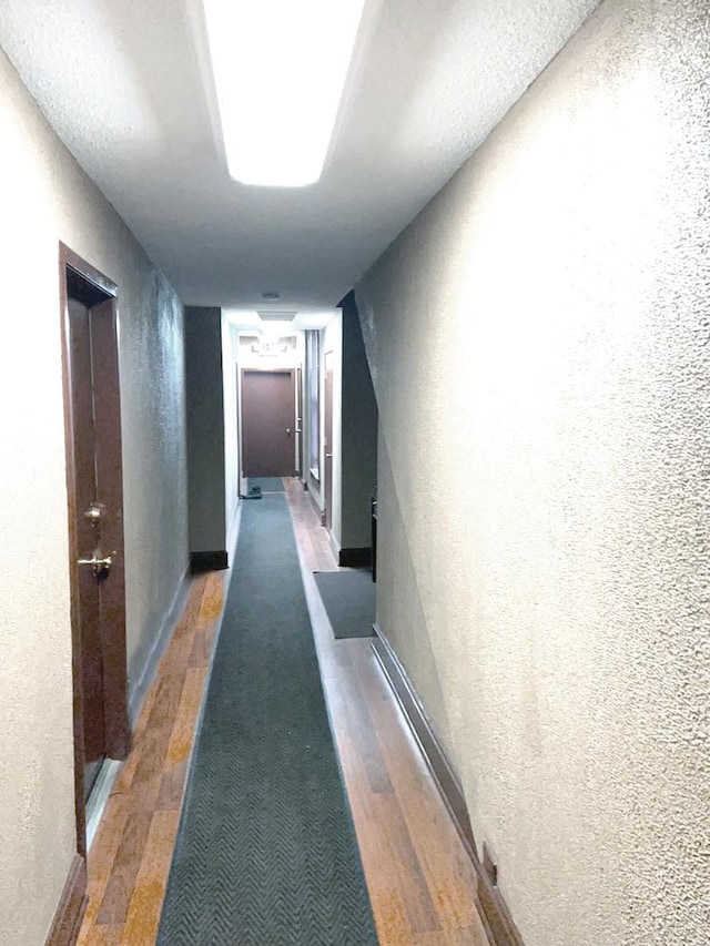 hall featuring baseboards, a textured wall, and wood finished floors