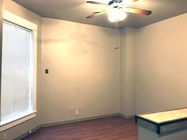 spare room featuring dark wood-type flooring, a ceiling fan, and baseboards