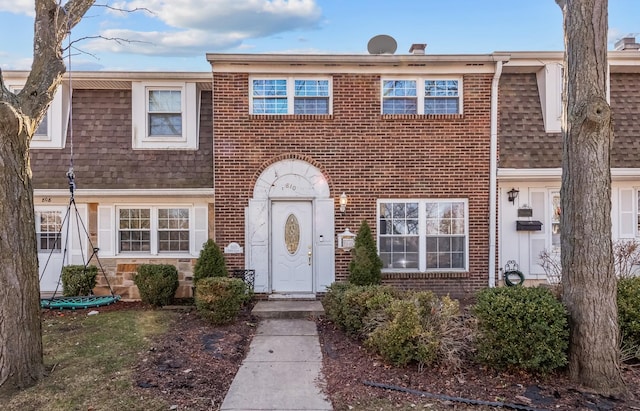 townhome / multi-family property with mansard roof, brick siding, and a shingled roof