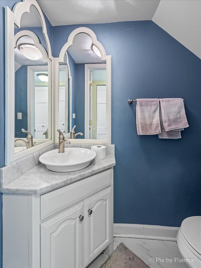 half bath featuring baseboards, toilet, vaulted ceiling, marble finish floor, and vanity