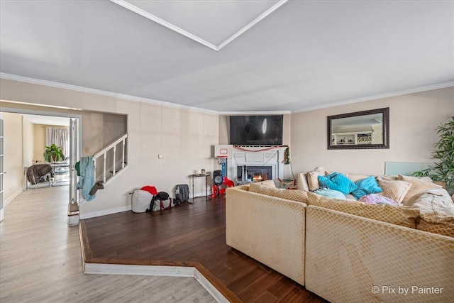 living area featuring a glass covered fireplace, stairs, crown molding, and wood finished floors