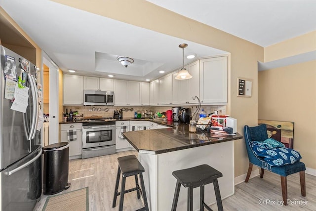 kitchen featuring a peninsula, appliances with stainless steel finishes, a kitchen bar, dark countertops, and backsplash