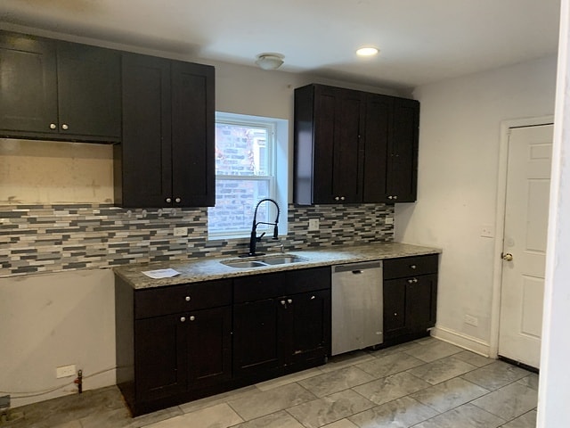 kitchen with stainless steel dishwasher, decorative backsplash, dark cabinetry, and a sink