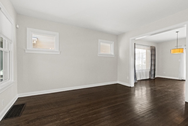 empty room featuring visible vents, baseboards, and dark wood-type flooring