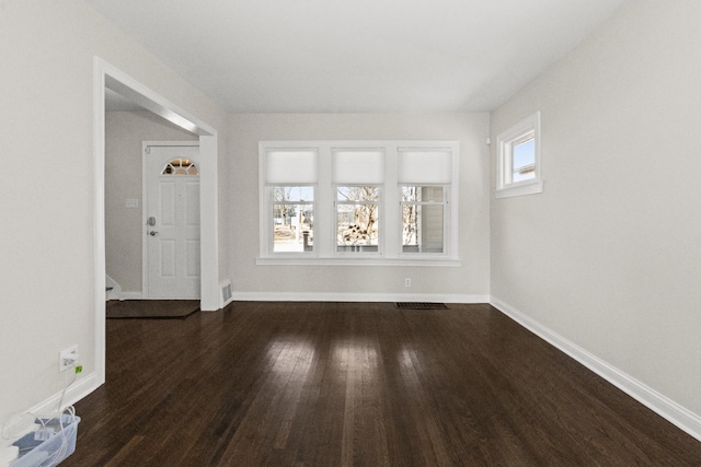 empty room with visible vents, dark wood-type flooring, and baseboards