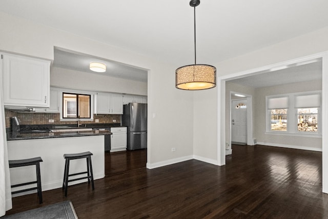 kitchen with dark countertops, dark wood-style floors, white cabinetry, freestanding refrigerator, and a peninsula