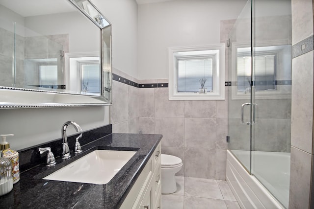 bathroom featuring tile patterned floors, toilet, tile walls, enclosed tub / shower combo, and vanity