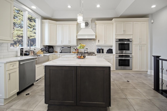 kitchen featuring decorative backsplash, a raised ceiling, premium range hood, and stainless steel appliances