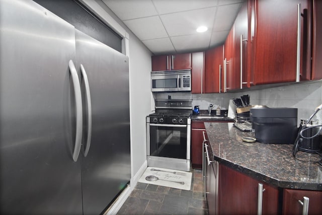 kitchen with tasteful backsplash, a drop ceiling, dark stone countertops, appliances with stainless steel finishes, and reddish brown cabinets