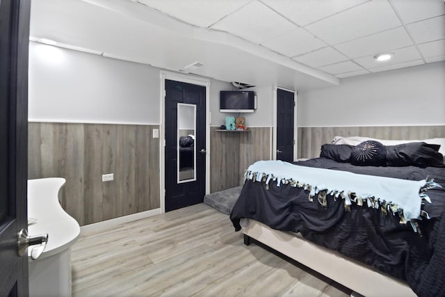 bedroom featuring a wainscoted wall, a paneled ceiling, wooden walls, and wood finished floors