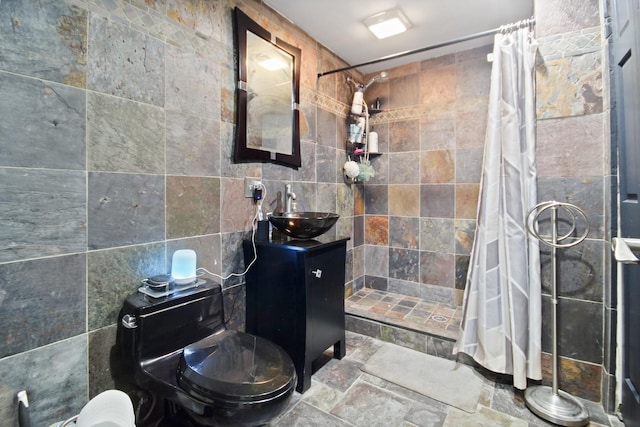 bathroom featuring tile walls, stone tile floors, vanity, and a tile shower