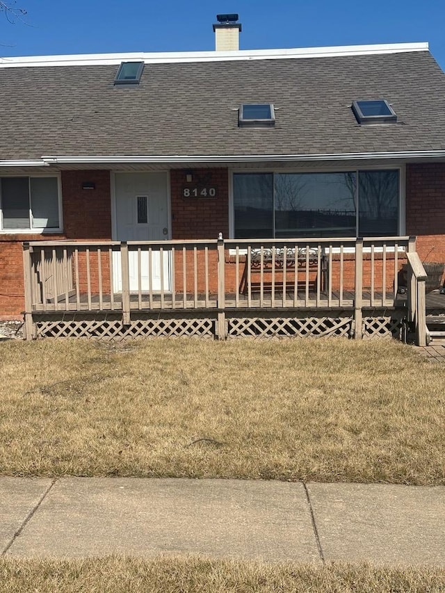 view of front facade featuring brick siding, a chimney, and a front lawn