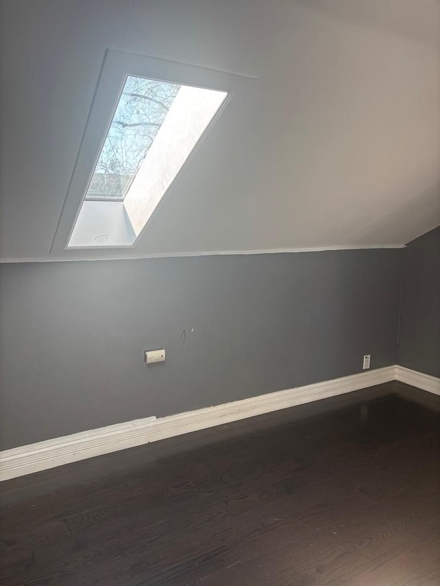 additional living space with lofted ceiling with skylight, wood finished floors, and baseboards