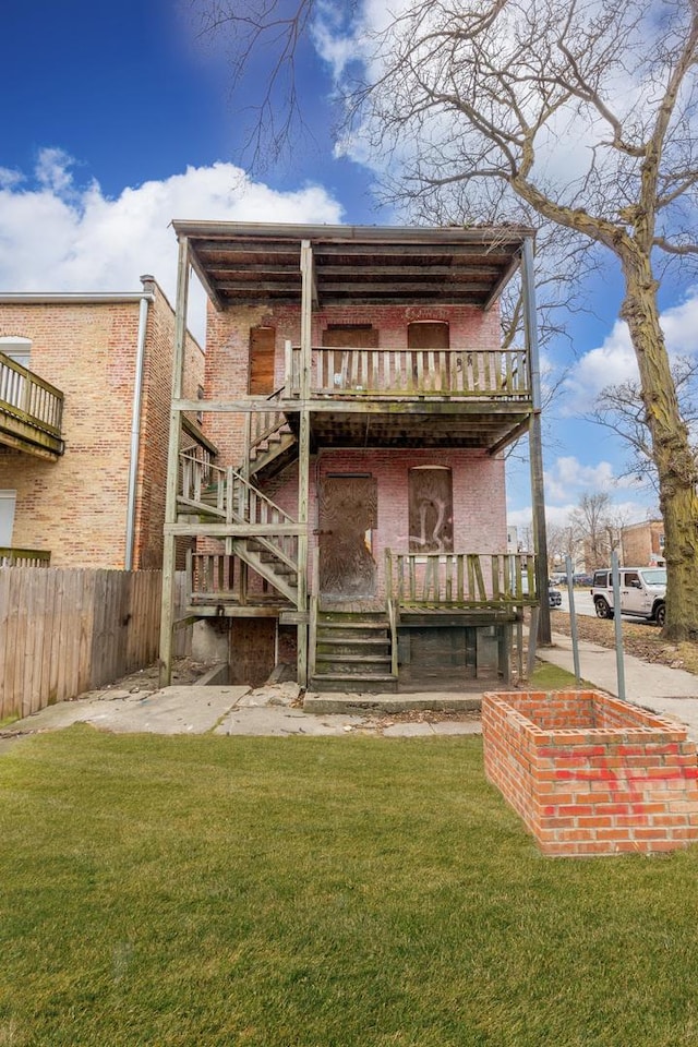 back of house featuring brick siding, a lawn, stairs, and fence